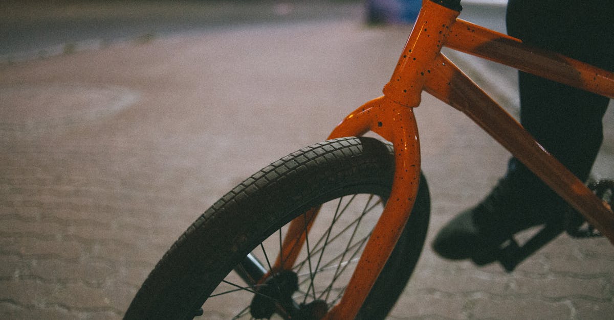 A close-up view of an orange BMX bike tire and fork on a pavement at evening.